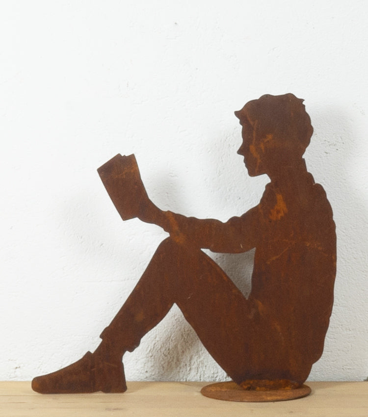 Uomo seduto che sta leggendo in corten